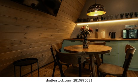 A warm and inviting A-frame cabin features a round wooden table with chairs, a small kitchen, and ambient lighting creating a serene atmosphere
