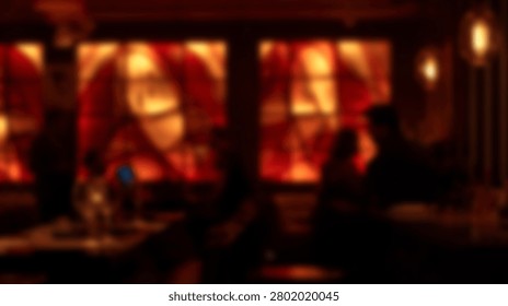 A warm and inviting bar interior, featuring a large abstract stained glass window illuminated from behind, with silhouetted patrons enjoying the atmosphere.
