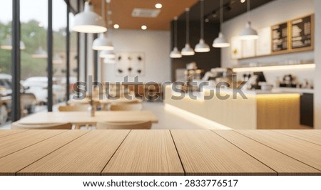 A warm and inviting cafe interior featuring wooden tables, chairs, and a modern bar counter with soft lighting. The background shows a blurred view of the seating area and the exterior.