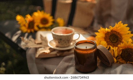 A warm, inviting composition featuring a lit candle, a cup of tea, and sunflowers, perfect for fall or relaxation.