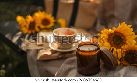 A warm, inviting composition featuring a lit candle, a cup of tea, and sunflowers, perfect for fall or relaxation.