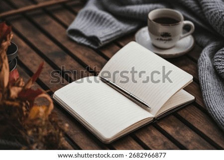 A warm and inviting scene featuring an open notebook, a cup of coffee, and a soft blanket on a rustic wooden surface.