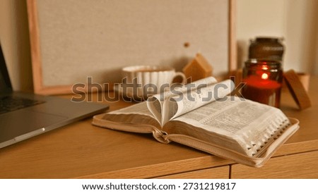 A warm and inviting scene featuring an open book with pages folded into a heart, alongside a laptop, coffee cup, and lit candle on a wooden desk