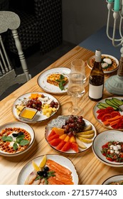 A warm and inviting table displays an array of colorful dishes, from fresh fruits and seafood to savory cheeses, alongside a chilled bottle of wine. Friends enjoy their culinary feast