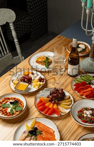A warm and inviting table displays an array of colorful dishes, from fresh fruits and seafood to savory cheeses, alongside a chilled bottle of wine. Friends enjoy their culinary feast