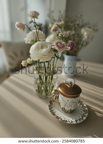A warm and inviting tea time setting bathed in afternoon sunlight, featuring a delicate ranunculus floral arrangement and a cup of coffee. This high-resolution image captures a serene and elegant