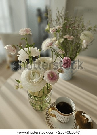 A warm and inviting tea time setting bathed in afternoon sunlight, featuring a delicate ranunculus floral arrangement and a cup of coffee. This high-resolution image captures a serene and elegant atmo