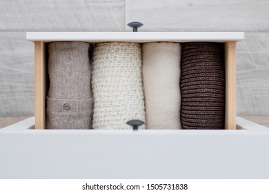warm knitted women's clothing in brown  white   beige colors in the drawer the chest drawers the background the wooden floor  top view