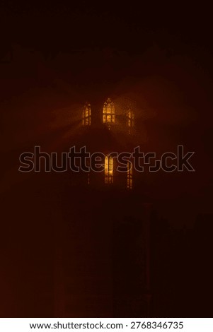 Warm light shining through tower windows in dense fog creates dramatic glowing rays and mysterious atmosphere. Moody night scene with soft haze and cinematic lighting, suitable for concepts of solitude, mystery and calm.