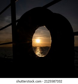 The warm light from the sun passes through the circle steel hole on the boat. It has a 1x1 ratio and shows a sea ware surface.