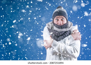 Warm. A man in a white sweater in a winter knitted hat and scarf stands under the falling snow. Snowfall. Winter. A person freezes in cold weather. - Shutterstock ID 2087251894