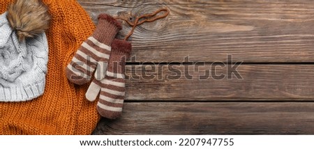 Warm mittens with knitted sweater and hat on wooden background with space for text