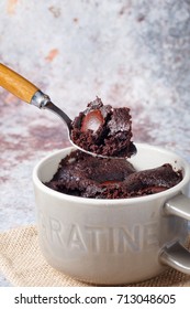 Warm Molten Melty Chocolate Chip Cocoa Coffee Mug Microwave Cake In Ceramic Mug Cup On Rustic Table Cloth Napkin Against Cement Floor Wall With Wooden Silver Spoon