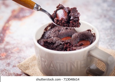 Warm Molten Melty Chocolate Chip Cocoa Coffee Mug Microwave Cake In Ceramic Mug Cup On Rustic Table Cloth Napkin Against Cement Floor Wall With Wooden Silver Spoon