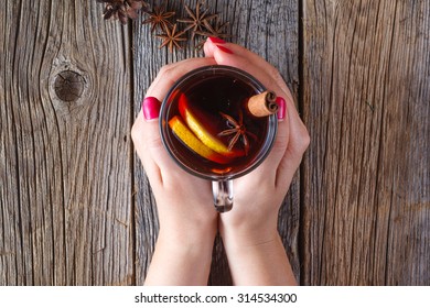 Warm Mulled Wine In Female Hands, Spices On Weathered Wooden Table. Top View