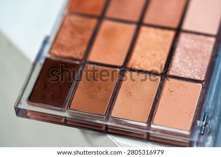 Warm neutral eyeshadow palette with multiple shades of brown bronze and peach arranged in grid. Beauty routine concept
