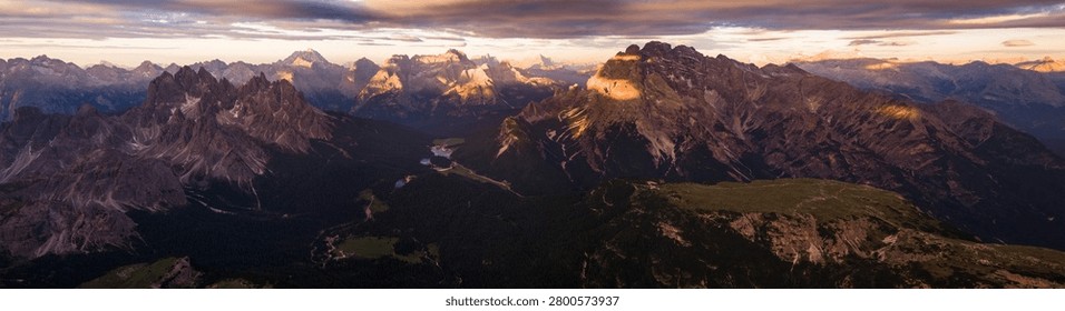Warm orange sunset illuminates the dramatic peaks and valleys of the Dolomites, creating an atmospheric alpine landscape with layered mountain silhouettes in Italy.