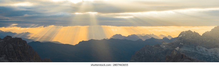 Warm orange sunset illuminates the dramatic peaks and valleys of the Dolomites, creating an atmospheric alpine landscape with layered mountain silhouettes in Italy.