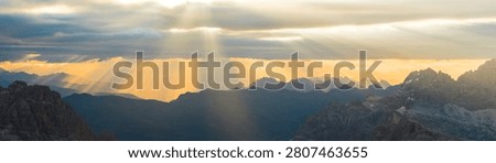 Warm orange sunset illuminates the dramatic peaks and valleys of the Dolomites, creating an atmospheric alpine landscape with layered mountain silhouettes in Italy.