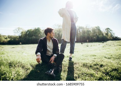 Warm portrait of couple in backlight with glare of sun in lens. The guy sits on the grass and smokes