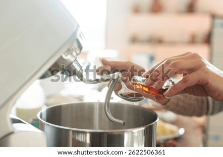 In a warm rustic kitchen, hands carefully add vanilla extract to a stand mixer, preparing to create fluffy Balkan Cozonac, a beloved Eastern European sweet bread filled with nuts and raisins