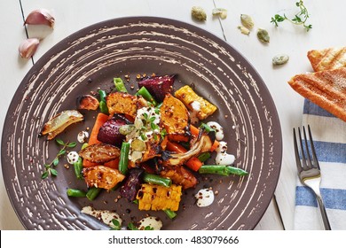 Warm Salad With Roasted Vegetables (pumpkin, Carrots, Beetroot, Green Bean, Onion) With Spices And Cream Sauce On A White Wooden Table. 