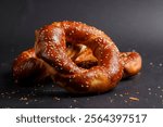 Warm, soft pretzels sprinkled with sesame seeds are arranged artfully against a dark background, highlighting their golden-brown color and texture.