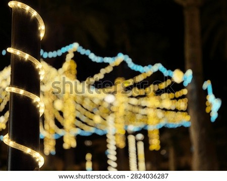 Warm spiral string lights wrap a dark pole in the foreground while softly blurred festive lights shimmer in the background at night.