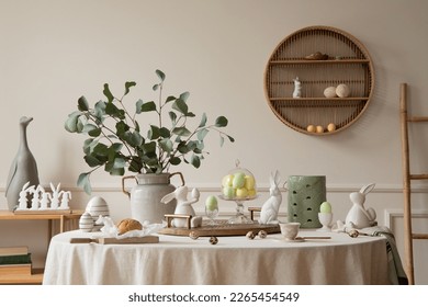 Warm and spring dining room interior with easter accessories, round table, vase with green leaves, cake, colorful eggs, rabbit sculpture and personal accessories. Home decor. Template. 