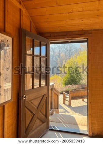 Warm sunlight streaming through an open wooden door, revealing a serene garden patio with lush greenery and autumn colors.