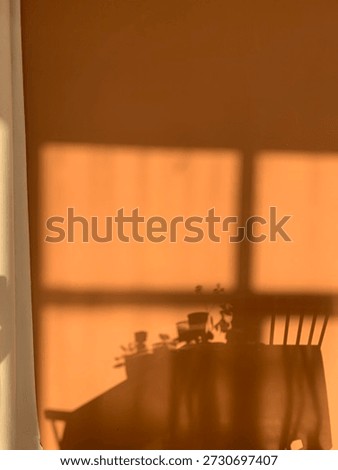 Warm sunlight window shadows on wall, cozy home interior background with copy space. Warm golden sunlight casting window shadows on wall with silhouettes of table and chairs. Minimal cozy home interior scene with soft light and large copy space. Atmospheric background for lifestyle, wellness, hygge, slow living, morning routine, banners, posters and social media design.