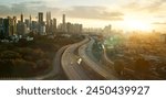 Warm sunset hues bathe a bustling city skyline and curving highway in golden light