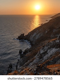 Warm sunset light over dramatic rocky coastline on Crete, Greece. Golden reflections on the sea, rugged cliffs and peaceful Mediterranean scenery with copy space.