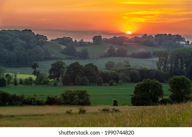 A warm sunset over the rolling hills in the south of Limburg near Maastricht. The last sunbeams give a golden colour over the hills and the field with wild yellow orchids. - Shutterstock ID 1990744820