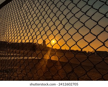 Warm sunset seen through a silhouette of a mesh fence. - Powered by Shutterstock