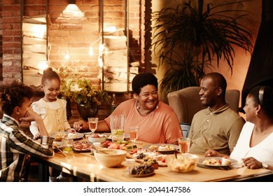 Warm Toned Portrait Of Big African-American Family Sitting At Table Outdoors And Enjoying Dinner Together At Evening