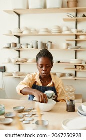 Warm toned portrait of creative African American woman decorating ceramics in pottery workshop, copy space