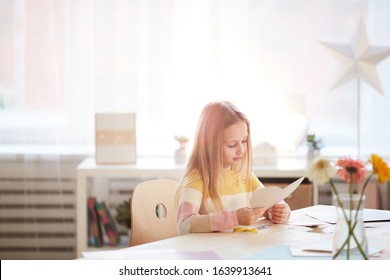 Warm Toned Portrait Of Cute Girl Making Holiday Card For Mothers Day Or Valentines Day While Sitting At Table In Cozy Home Interior, Copy Space