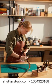 Warm Toned Portrait Of Female Craftsman Working With Leather In Tannery Shop