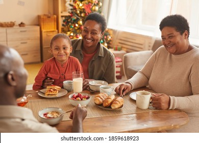 Warm toned portrait of happy African-American family enjoying tea and snacks while celebrating Christmas at home - Powered by Shutterstock