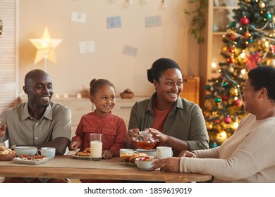 Warm toned portrait of happy African-American family enjoying tea and snacks while celebrating Christmas at home in cozy home interior - Powered by Shutterstock