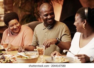 Warm toned portrait of happy African-American family enjoying dinner together outdoors at evening