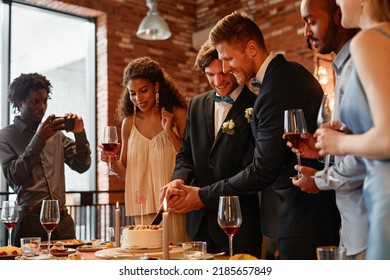 Warm Toned Portrait Of Happy Gay Couple Cutting Cake Together During Wedding Reception, Same Sex Marriage