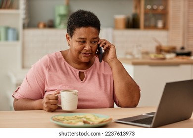 Warm toned portrait of senior woman talking on phone while enjoying breakfast in morning - Powered by Shutterstock