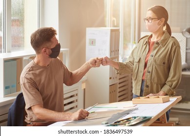 Warm Toned Portrait Of Two Colleagues Wearing Masks Bumping Fists As Contactless Greeting In Post Pandemic Office