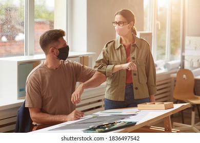 Warm Toned Portrait Of Two Colleagues Wearing Masks Bumping Elbows As Contactless Greeting In Post Pandemic Office