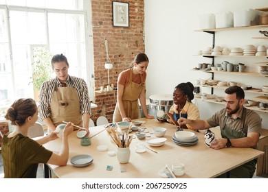 Warm toned shot of creative group of people decorating ceramics in pottery workshop, copy space - Powered by Shutterstock