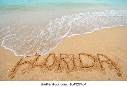 A warm tropical beach with blue water and waves and Florida written in the sand