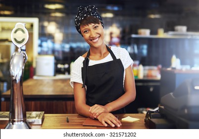 Warm welcoming young business entrepreneur standing behind the counter in her cafe giving the camera a beaming smile of welcome - Powered by Shutterstock