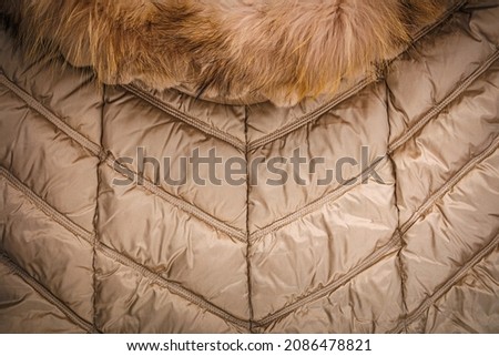Warm winter jacket with modern quilted pattern. Gold Down jacket with fur hooded collar.  Winter season fashion background. 